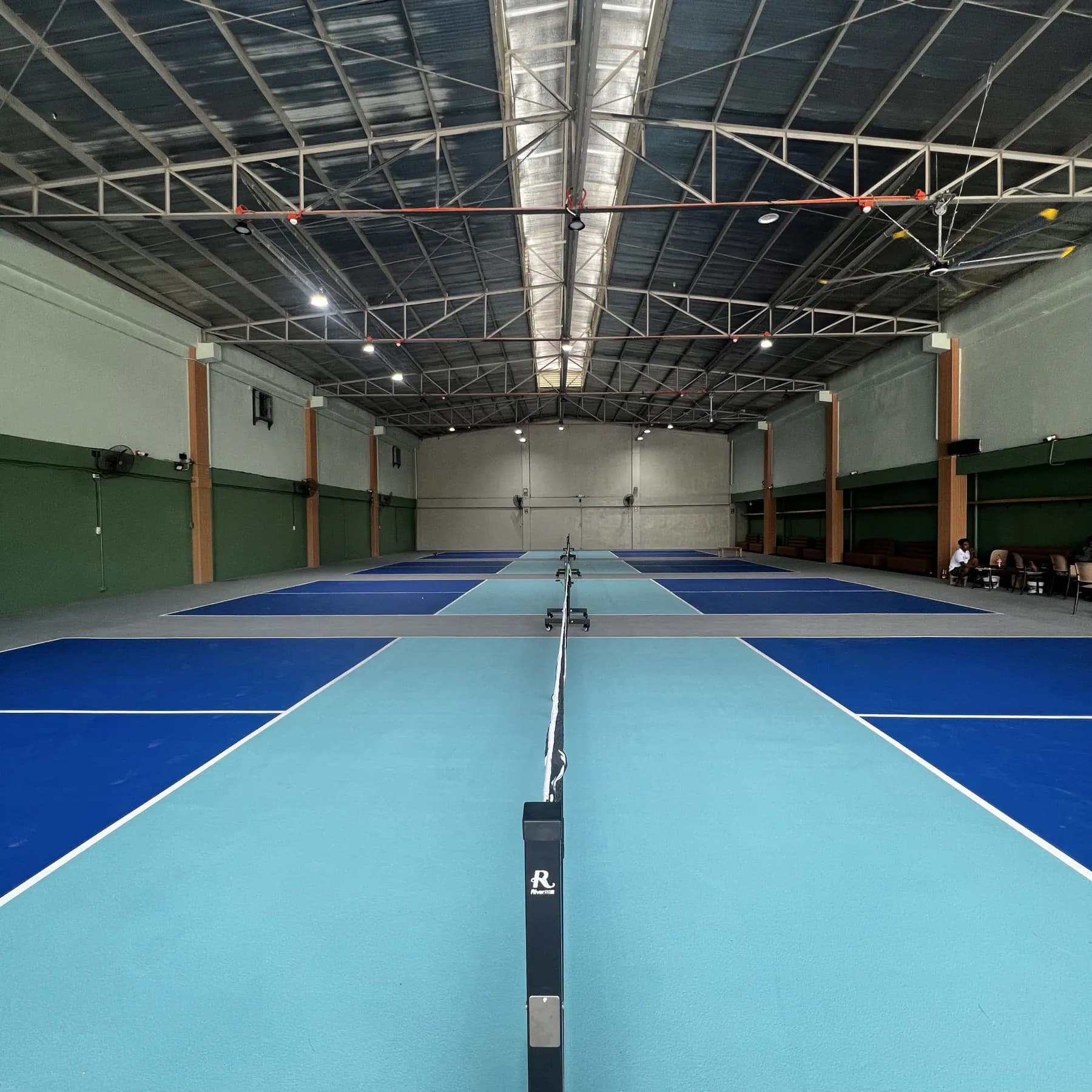 Indoor blue pickleball courts viewed along the center net